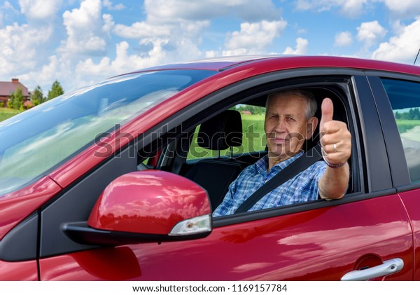 Old\
contented man driving a car showing his\
thumb