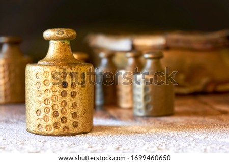 Old copper brass scale weights with calibration marks on wooden table with flour in a bakery. Image with selective focus.
