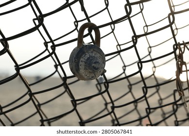 Old corroded combination lock that has been locked onto a chain link fence for years. Sunrise and beach in the background are blurred.