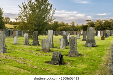 Old country cemetery with old gravestones surrounded by stone wall, green fields and trees at golden hour sunset  - Powered by Shutterstock