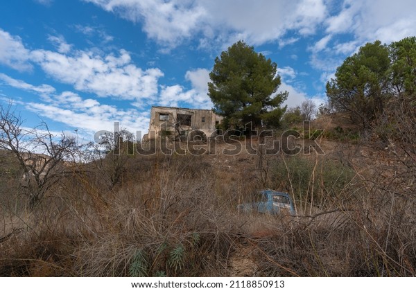 old country house in a mountainous area in the\
south of Granada in Spain, there are trees and bushes, there is an\
old car, the sky is cloudy