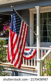 Old country middle American rural house with a wooden porch and white railings celebrating Independence Day with United States Flag and banner.