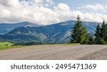 old country road in carpathian mountains of ukraine. landscape in early autumn. trees on the roadside in evening light. blue sky with fluffy clouds above the distant ridge