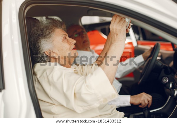 Old couple in a car salon.\
Family buying the car. Elegant woman with her husband. Senior by a\
car.