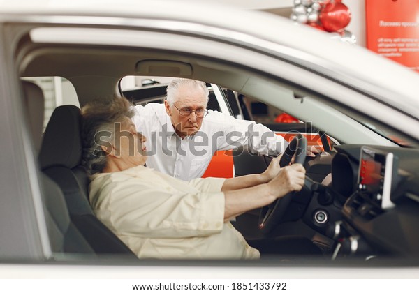 Old couple in a car salon.\
Family buying the car. Elegant woman with her husband. Senior by a\
car.