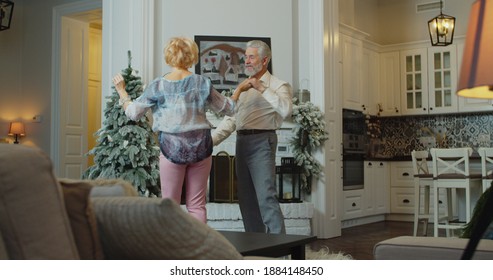 The Old Couple Dancing Near The Christmas Tree. Cheerful Senior Caucasian Couple Dancing In Front Of Christmas Tree.