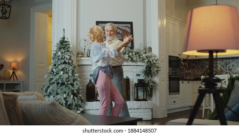 The Old Couple Dancing Near The Christmas Tree. Cheerful Senior Caucasian Couple Dancing In Front Of Christmas Tree.