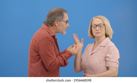 Old Couple Fighting And Shouting At Each Other During A Heated Argument. Old Couple Facing Conflicts While Living In A Relationship. Fighting Concept. Blue Background.