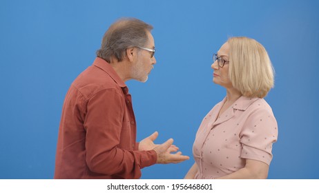 Old Couple Fighting And Shouting At Each Other During A Heated Argument. Old Couple Facing Conflicts While Living In A Relationship. Fighting Concept. Blue Background.