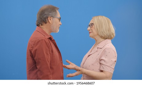 Old Couple Fighting And Shouting At Each Other During A Heated Argument. Old Couple Facing Conflicts While Living In A Relationship. Fighting Concept. Blue Background.