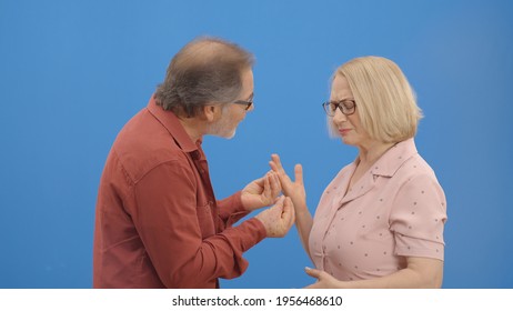 Old Couple Fighting And Shouting At Each Other During A Heated Argument. Old Couple Facing Conflicts While Living In A Relationship. Fighting Concept. Blue Background.