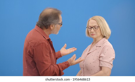 Old Couple Fighting And Shouting At Each Other During A Heated Argument. Old Couple Facing Conflicts While Living In A Relationship. Fighting Concept. Blue Background.