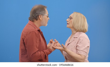 Old Couple Fighting And Shouting At Each Other During A Heated Argument. Old Couple Facing Conflicts While Living In A Relationship. Fighting Concept. Blue Background.