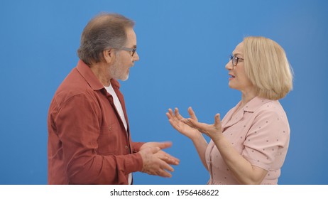 Old Couple Fighting And Shouting At Each Other During A Heated Argument. Old Couple Facing Conflicts While Living In A Relationship. Fighting Concept. Blue Background.