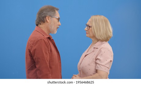 Old Couple Fighting And Shouting At Each Other During A Heated Argument. Old Couple Facing Conflicts While Living In A Relationship. Fighting Concept. Blue Background.