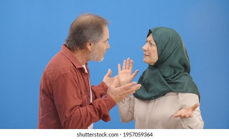 Old Couple Fighting And Shouting At Each Other During A Heated Argument. Old Couple Facing Conflicts While Living In A Relationship. Fighting Concept. Blue Background.