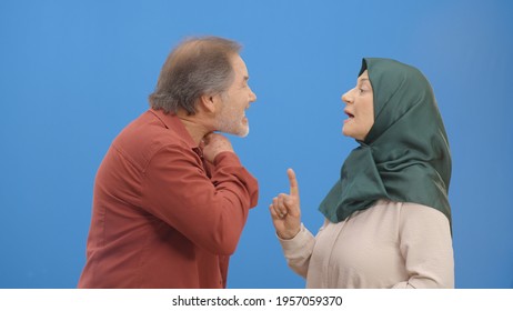 Old Couple Fighting And Shouting At Each Other During A Heated Argument. Old Couple Facing Conflicts While Living In A Relationship. Fighting Concept. Blue Background.S