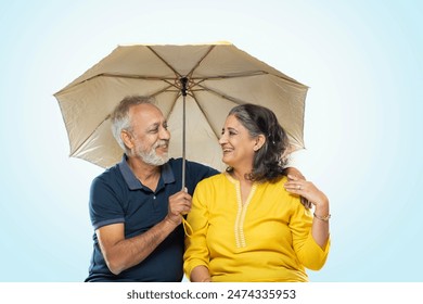 AN OLD COUPLE HAPPILY LOOKING AT EACH OTHER WHILE SITTING UNDER AN UMBRELLA
 - Powered by Shutterstock