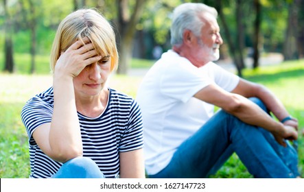 Old Couple Ignoring And Not Speaking Each Other Sitting On Grass In The Garden.Unhappy Old Couple.Angry Senior Couple Having An Argument In The Park.Marriage In Crisis.Relationship Problems.