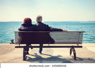 Old couple of lovers on a bench. Back view of romantic seniors dating in front of the lake