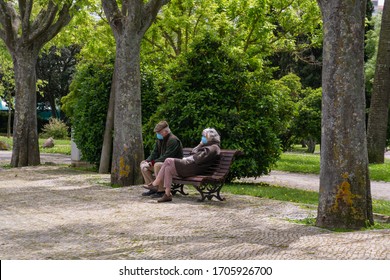 Old Couple With Masks Sitting In The Park During Coronavirus. Older People During Epidemic With Masks  On The Banch In Lisbon 13.04.2020