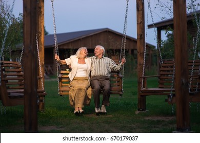 Old Couple On Porch Swing. Man And Woman, Evening.