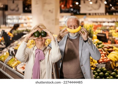 An old couple is playing silly faces with fruits at supermarket. - Powered by Shutterstock