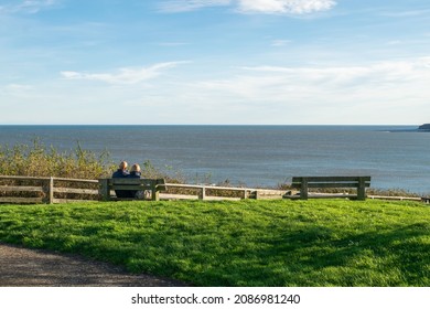 Old Couple Sit On Bench Enjoying The Sea View In England