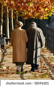 Old Couple Walking Along An Autumn Path Arm In Arm