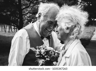 Old couple is walking in the green park. Grandmother and grandfather at their golden wedding anniversary celebration. Fifty years together love story. Grandma and grandpa kissing. Black and white.