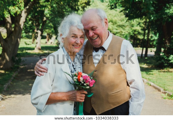 老夫婦在綠色公園散步 祖母和祖父在他們的黃金結婚週年慶祝活動 五十年一起長者愛情故事 奶奶和爺爺都在笑庫存照片 立刻編輯