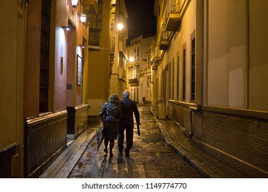 Old Couple Walking In Seville At Night, Spain