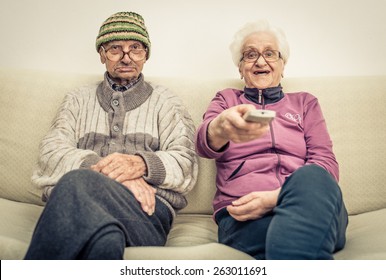 Old Couple Watching Television On The Couch In The Living Room. Concept About Aging, Old People, Entertainment, Humor And People