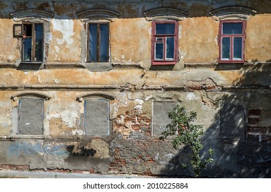 An old crumbling house. The windows of the first floor are walled up. On the second floor there are old wooden windows.