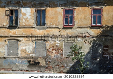 An old crumbling house. The windows of the first floor are walled up. On the second floor there are old wooden windows.
