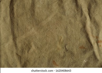 Old, crumpled and dirty khaki color tarpaulin, detailed texture. Fabric of a vintage army military or travel backpack for background. Worn natural sail cloth material with stains