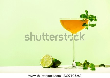 Old Cuban alcoholic cocktail drink with white rum, lime juice, sparkling wine, syrup, bitter, mint and ice. Lime green background, hard light, shadow pattern