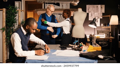 Old customer dressing up suit jacket in tailoring workshop, fitting clothes with custom made body measurements. Male client collaborating with couturiers team in fashion atelier. - Powered by Shutterstock