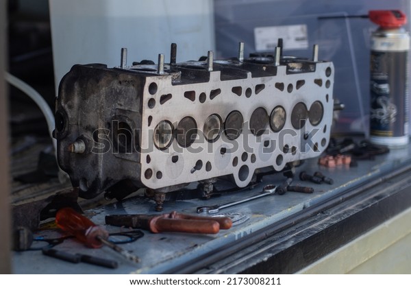 Old cylinder head of a 8V diesel engine\
sitting on a bench or atable. Visible combustion side of a cylinder\
head, just milled or\
straightened.