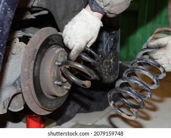 Old Damaged Coil Spring Parts In Hands On Broken Car Background - Vehicle Suspension Repair Workshop In Garage