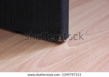 Old damaged edge of threadbare table on wooden floor background. Interior detail of broken worn out black wood table in the room
