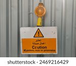 Old damaged maintenance in progress caution or warning text on sign board near construction site wall to prevent industrial accidents or hazards. Closeup side view.