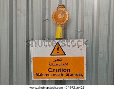 Old damaged maintenance in progress caution or warning text on sign board near construction site wall to prevent industrial accidents or hazards. Closeup side view.