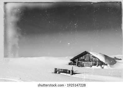 Old, damaged vintage retro style tundra landscape black and white photo. Wooden house with well covered with snow in the front. Lots of age marks, letters, scratches placed on the film tape surface. 
