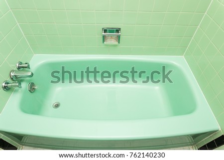 An old, dated green bathtub with green tiles.