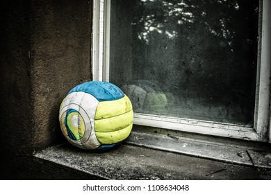 Old Deflated Volleyball In Blue And Yellow On Grunge Urban Background With Old Dirty Window