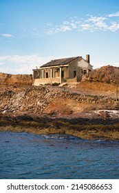 Old Deserted Fishermans House On A Small Island Close To Luderitz, Namibia  With The Dark Blue Sea In The Foreground On A Cold And Sunny Day 