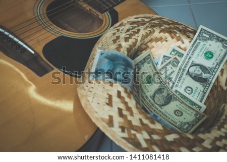 Old dirty acoustic guitar and multi currency money cash on weaving hat. 
