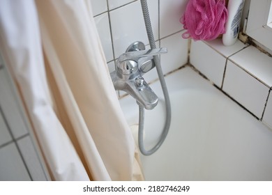 Old Dirty Bathtub, Shower Curtain, And Faucet In An Apartment Bathroom. Top View, White Faience Wall, No People.