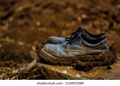 Old dirty boots on the rock, full of clay and mud at the boots.